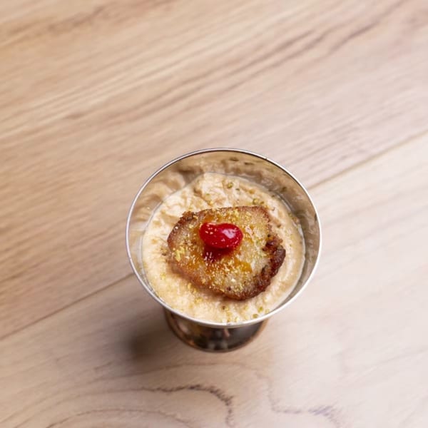 Overhead view of a dessert in a silver cup, featuring a fried pastry and red cherry.