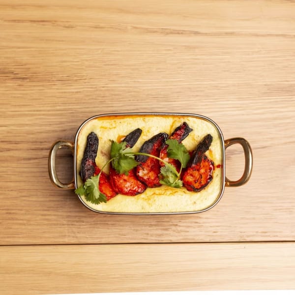 Creamy polenta topped with roasted red peppers and fresh cilantro in a gold-handled dish.