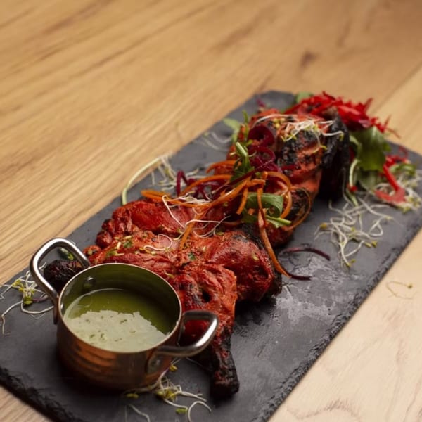 Tandoori chicken with green sauce and salad on a black slate plate.