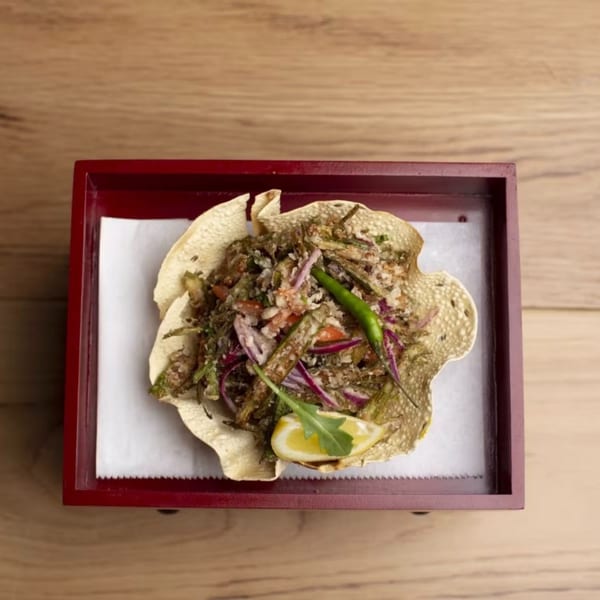 Indian dish with okra, red onions, and chili, served in a papadum bowl on a red tray.